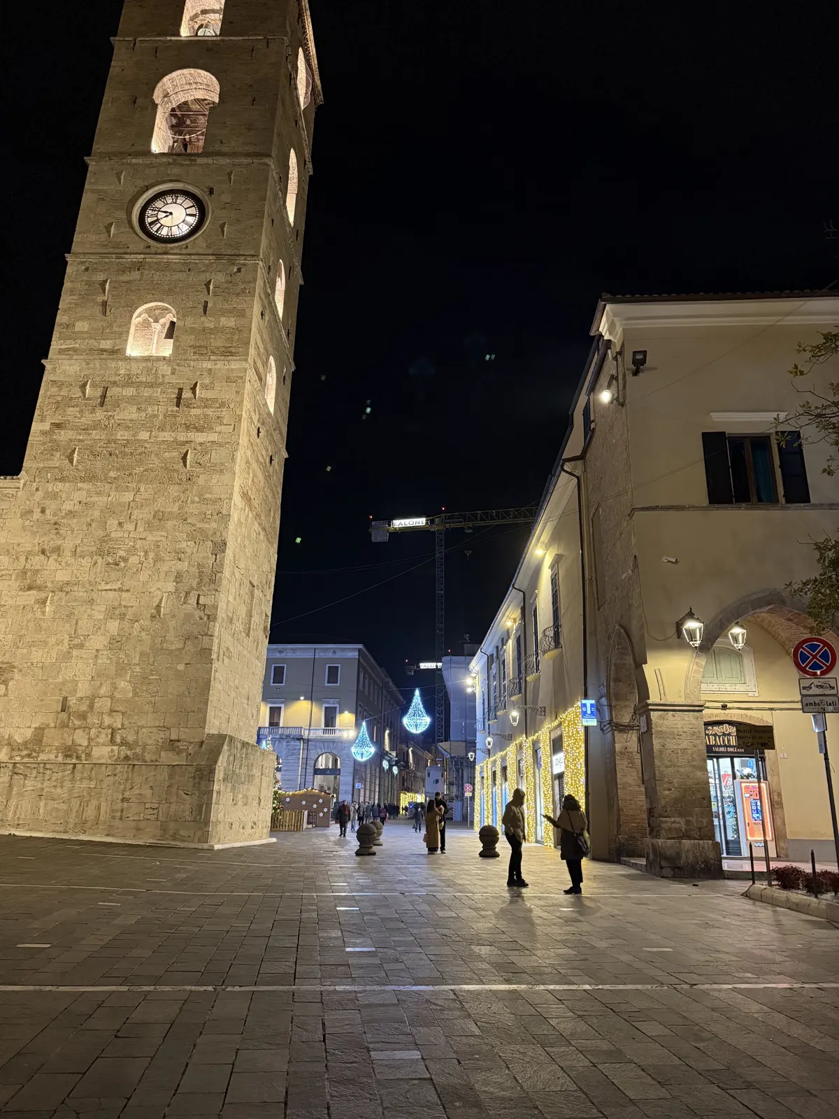 An illuminated clock tower beside a village street at night