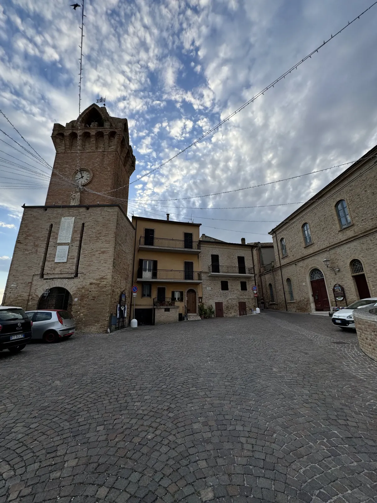 A cobbled historic square with a stone tower and surrounding buildings