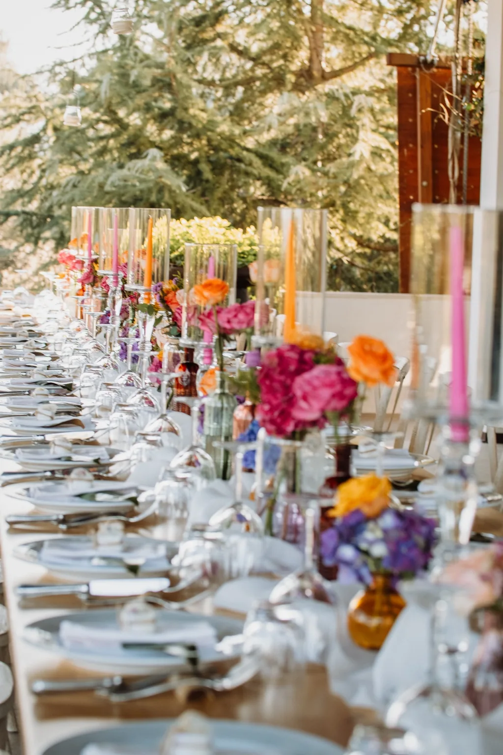 A long dining table set with colourful flowers, candles and glassware