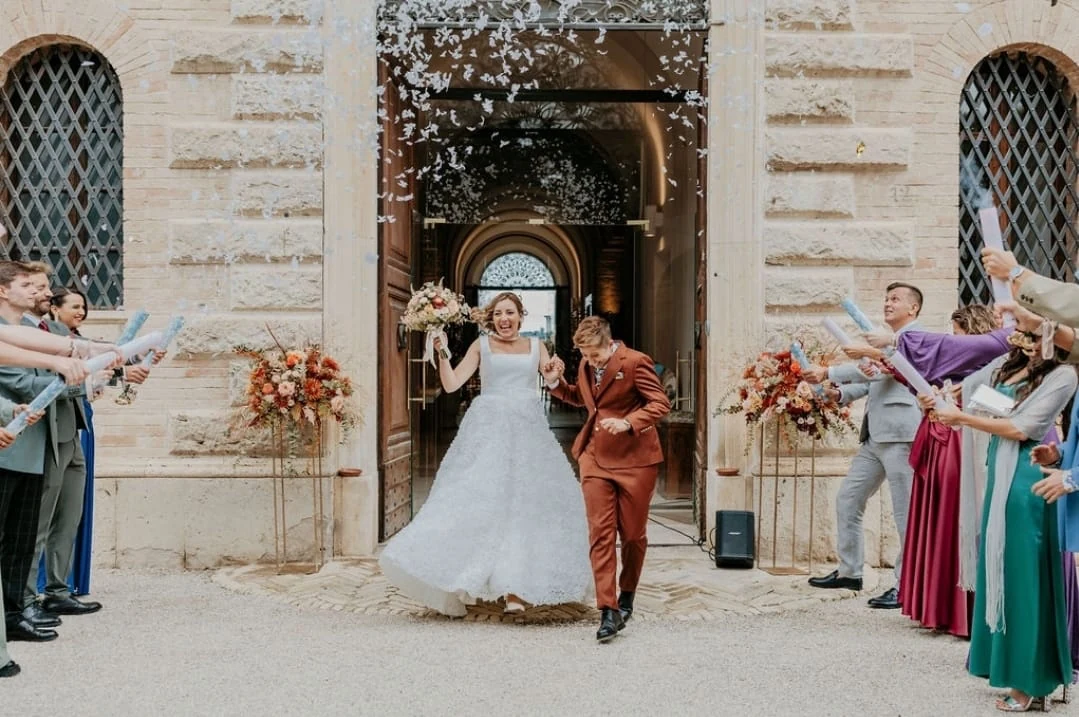 Claudia and Bruna walking out through confetti, smiling, with guests on either side
