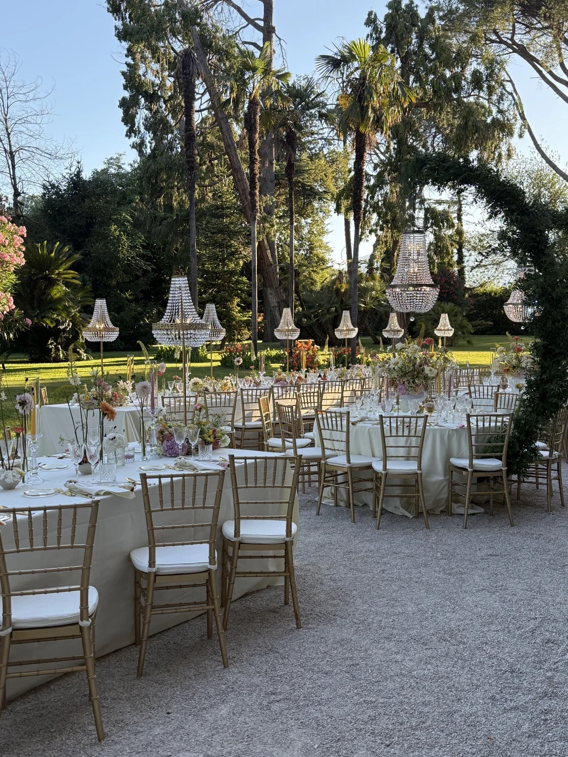 Wedding reception tables with flowers and suspended chandeliers in a palm-filled garden
