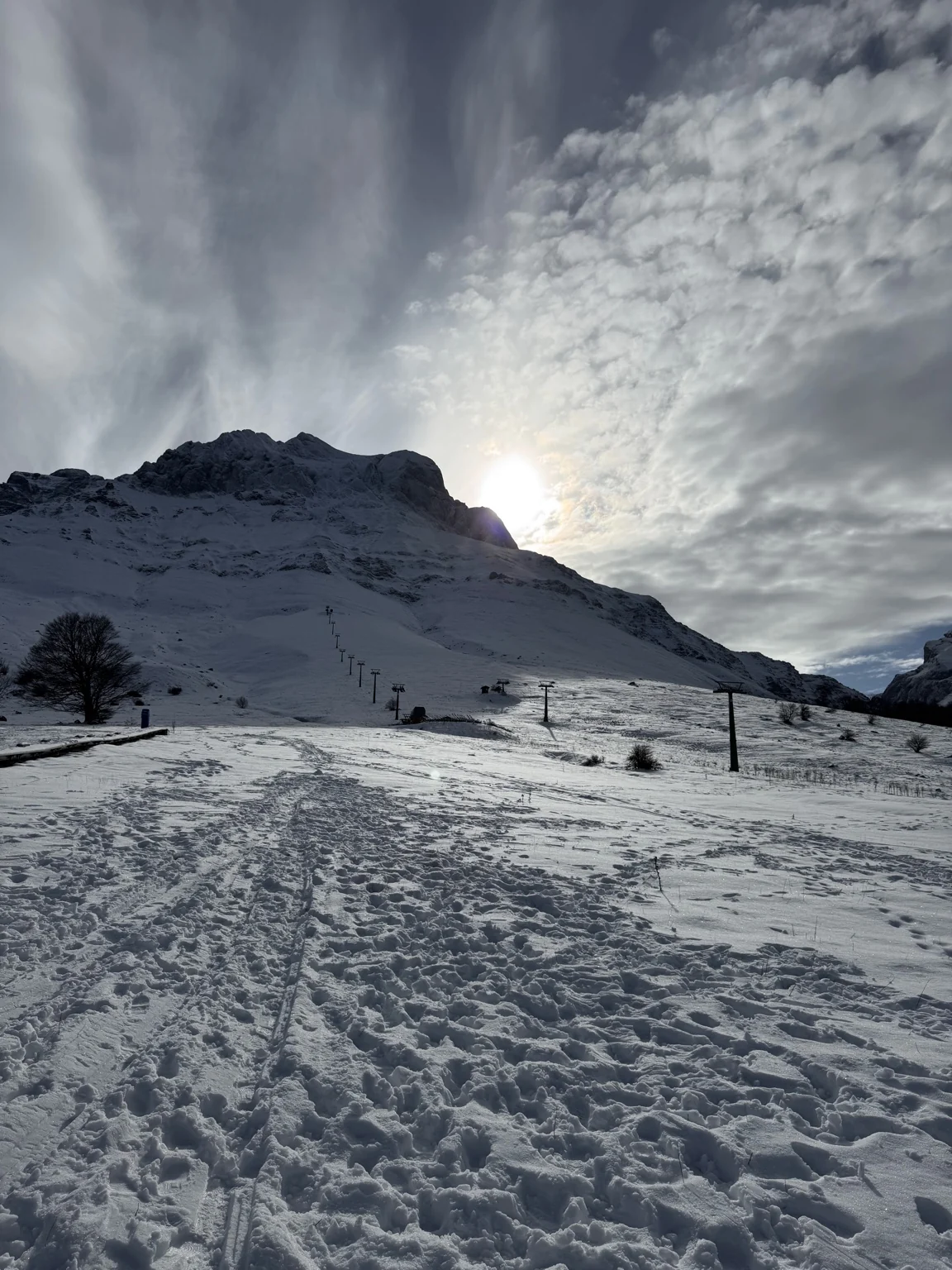 Snow-covered mountain slopes and ski lifts beneath a cloud-streaked sky